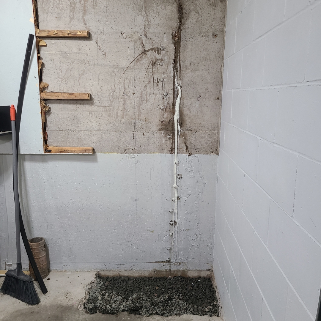 Same basement corner after crack injection, wall sealed and painted with gravel drainage at the base
