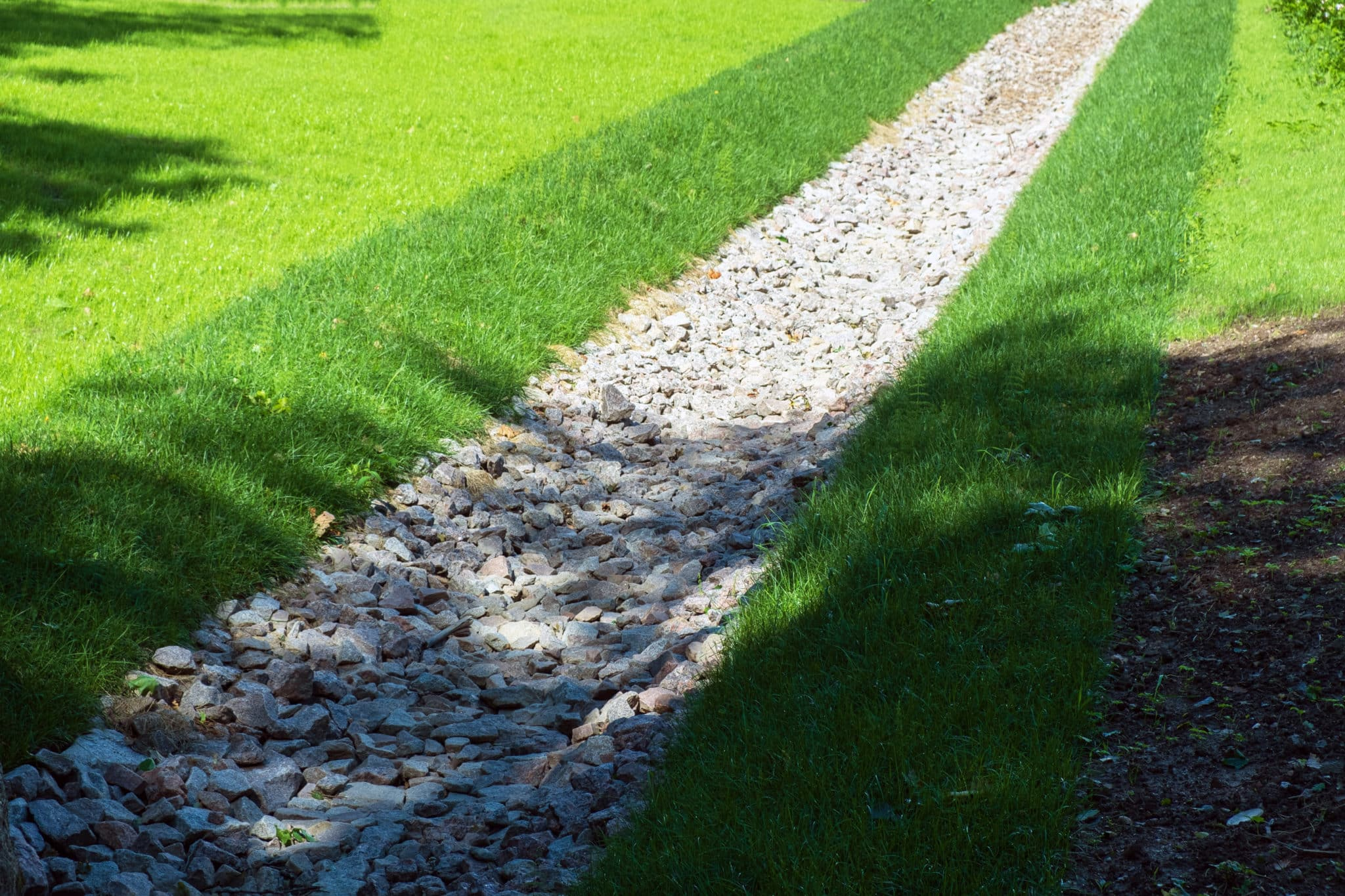 Finished rock drainage swale running through a healthy green lawn