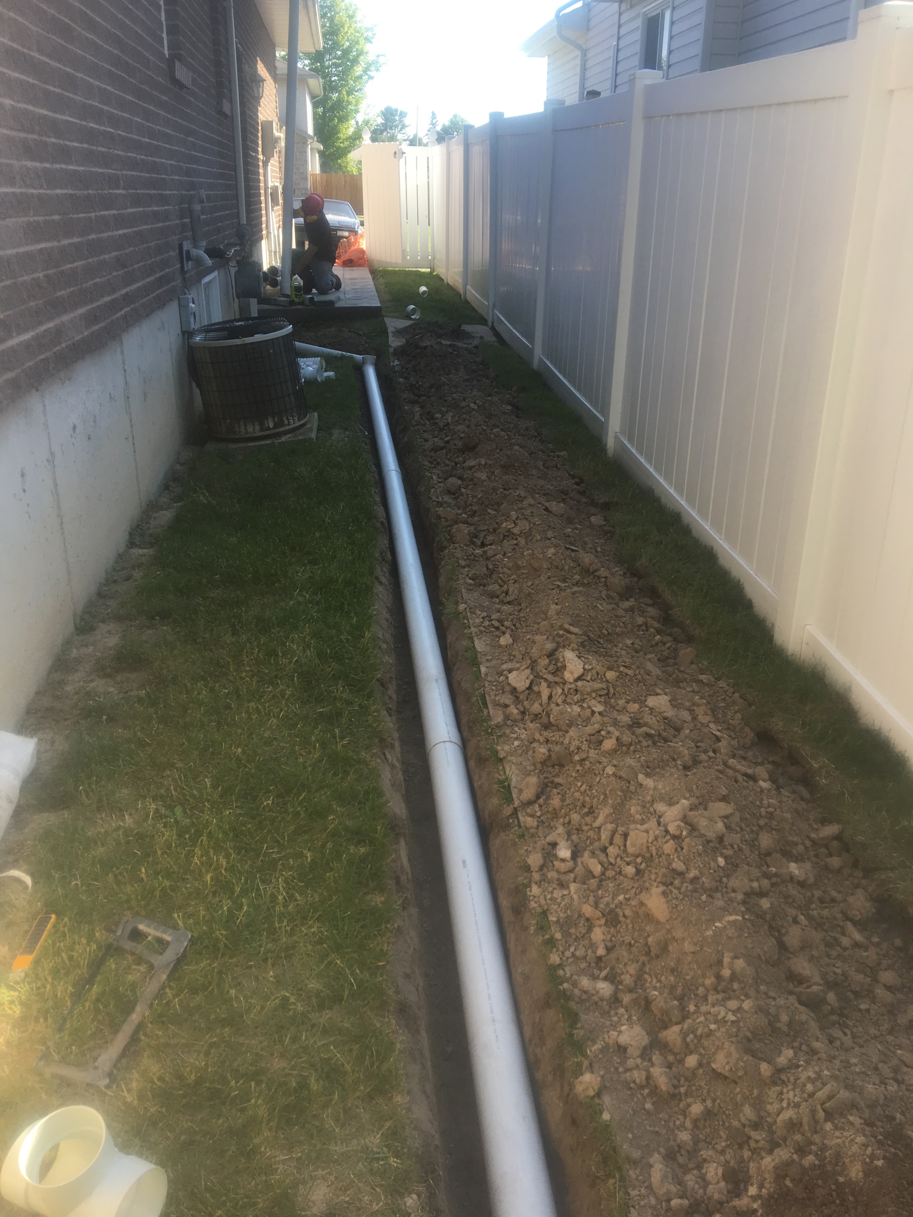 Drainage trench dug along a home foundation with PVC pipe being installed